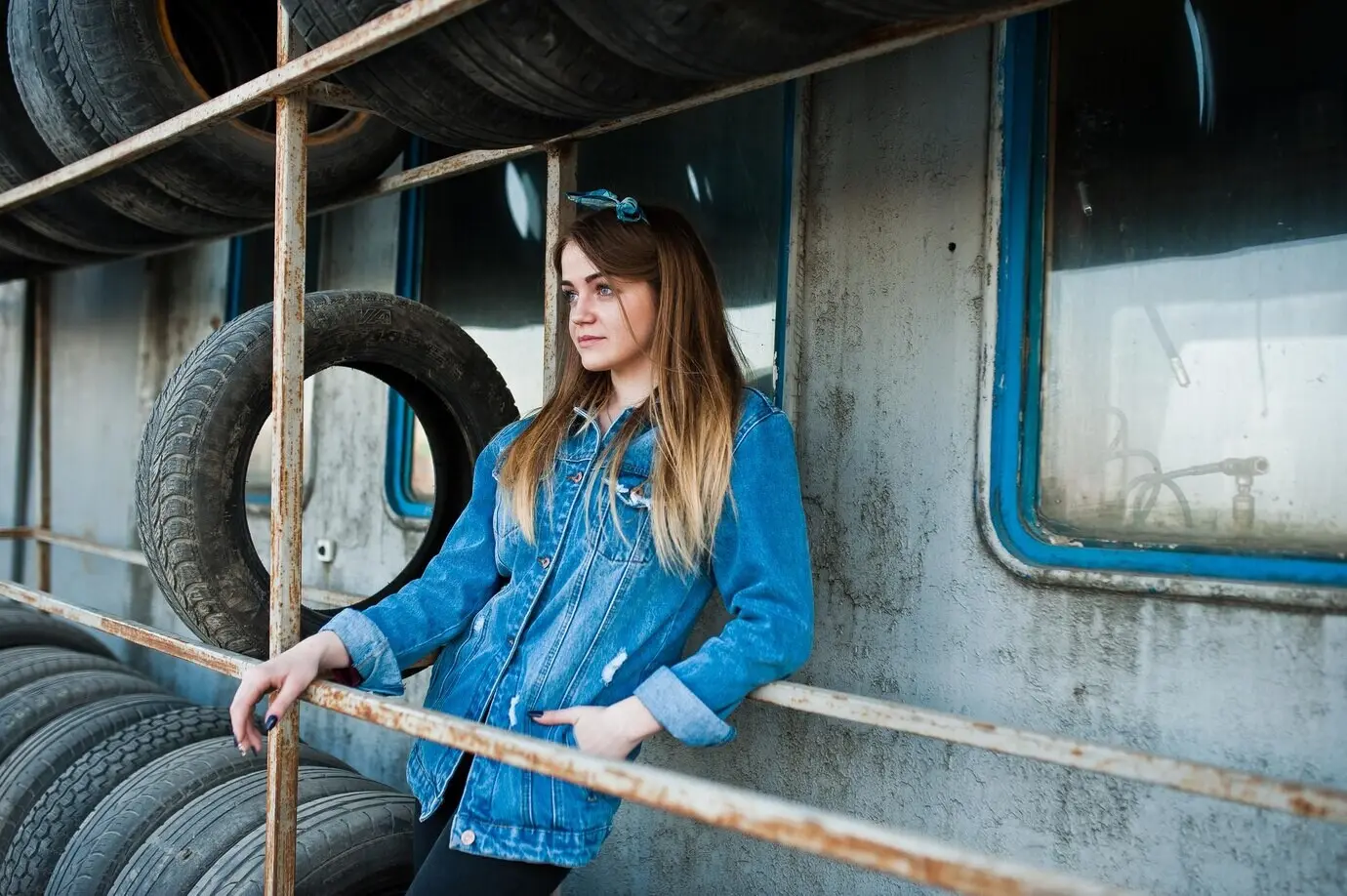 Jeune fille hipster avec une veste en jean et un foulard sur la tête, dans une zone de montage de pneus.
